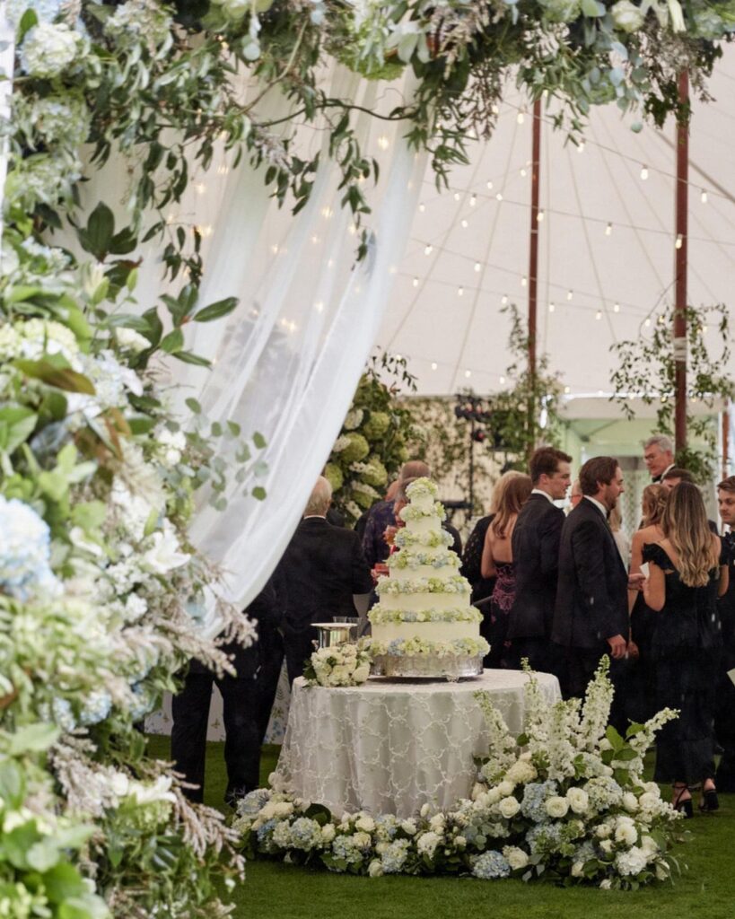 Multi-tiered white wedding cake on a lace table surrounded by white flowers