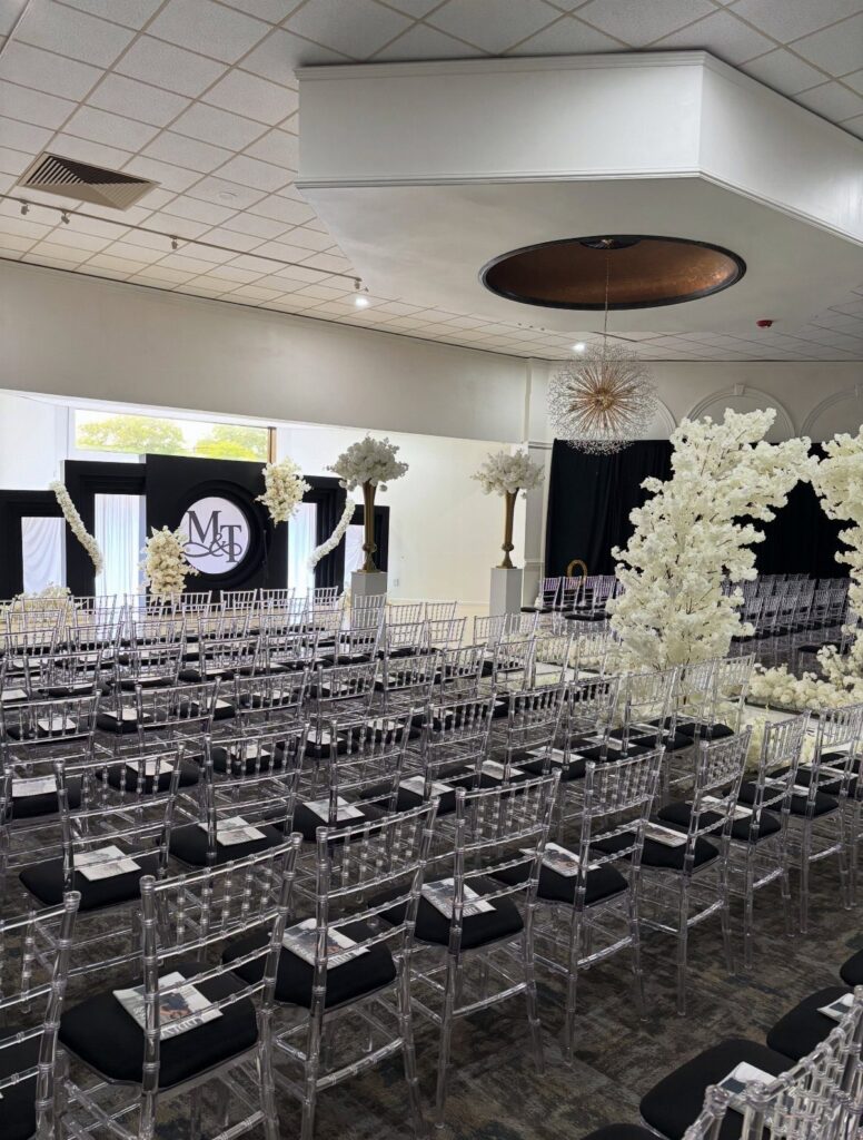 Indoor wedding venue setup with clear acrylic chairs and white floral decorations.