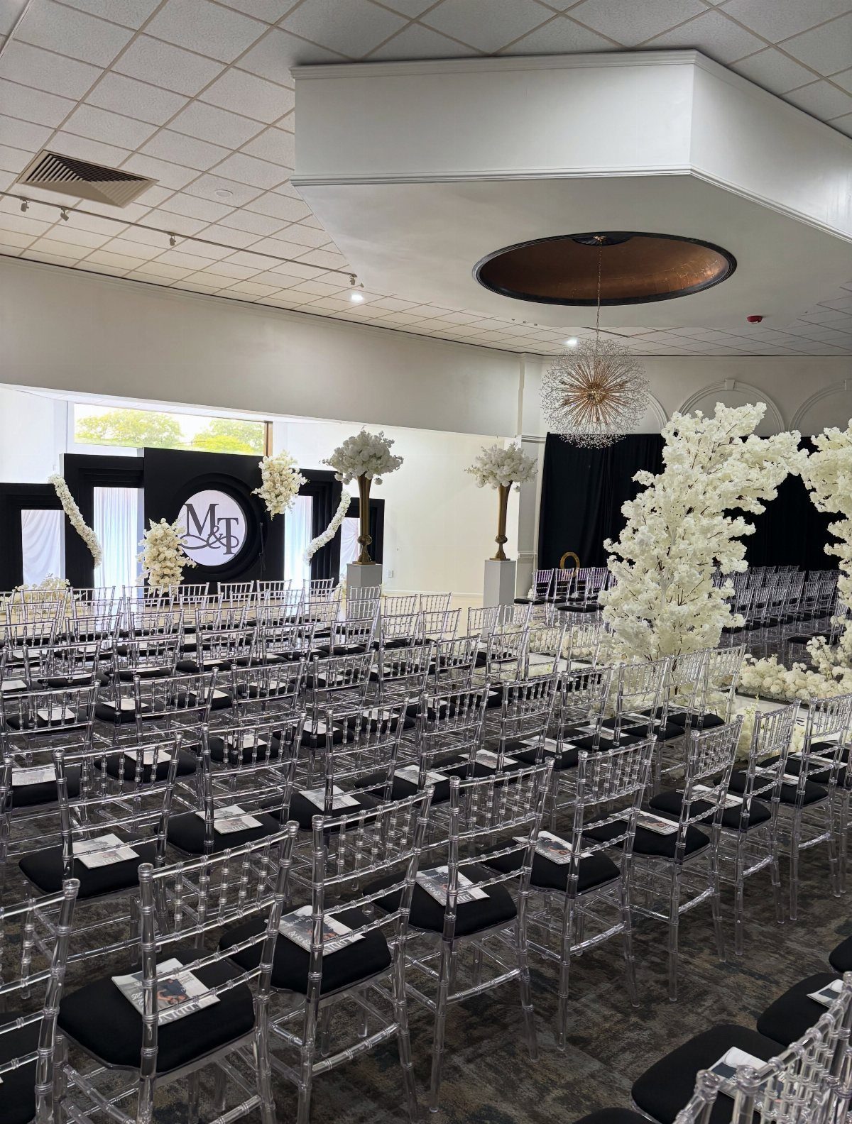 Indoor wedding venue setup with clear acrylic chairs and white floral decorations.