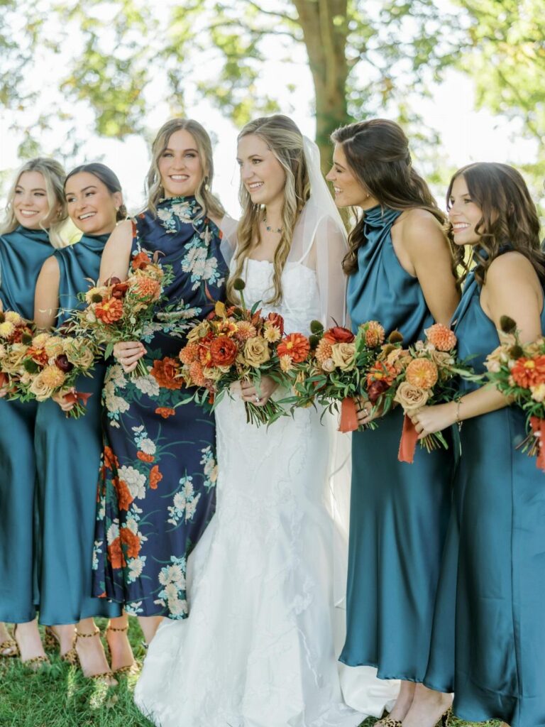 Bride and bridesmaids in blue dresses holding orange autumn bouquets in a park