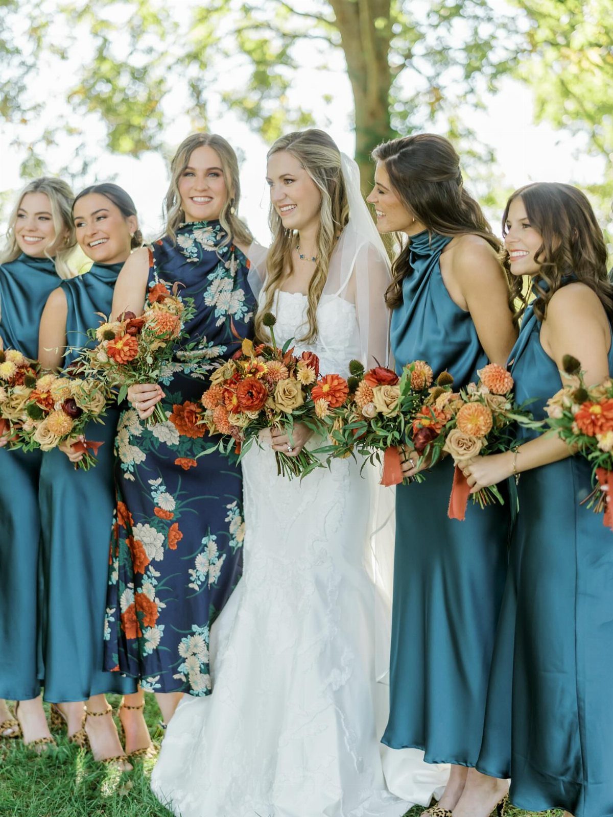 Bride and bridesmaids in blue dresses holding orange autumn bouquets in a park