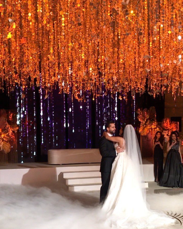 Bride and groom dancing on a foggy stage under golden hanging decorations.