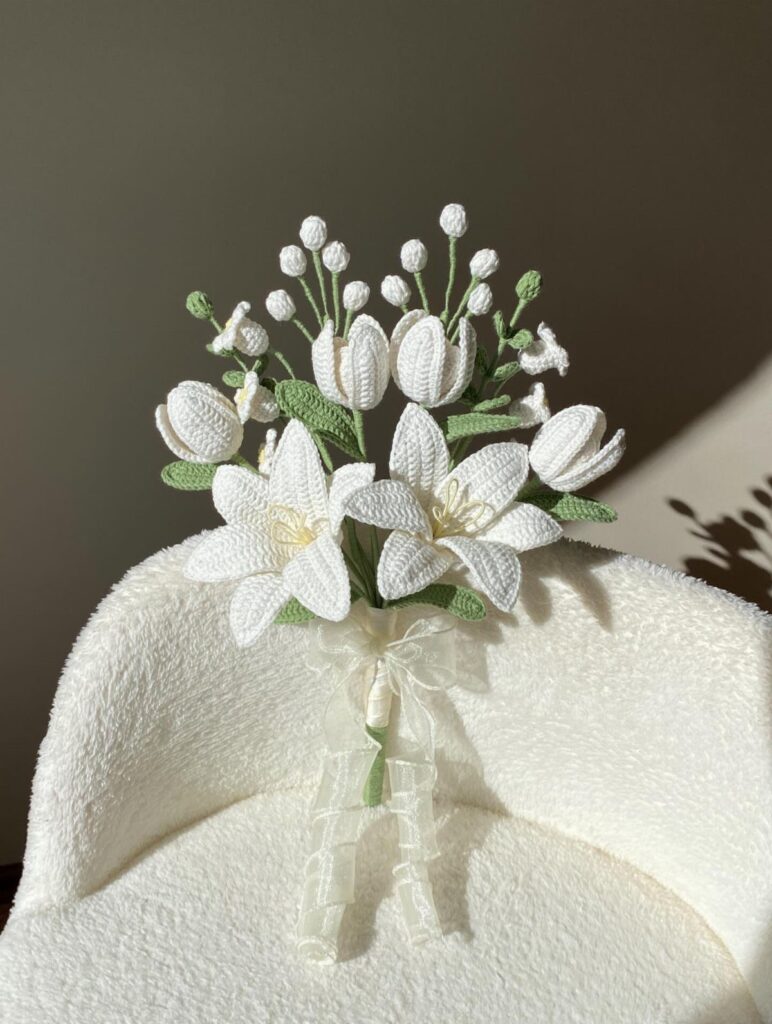White crocheted lily bouquet with green stems and a sheer ribbon on fabric