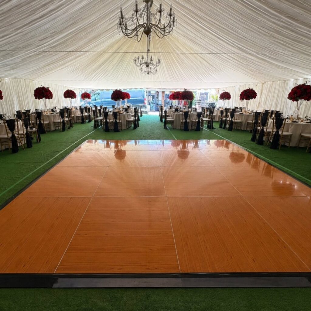 Polished wood dance floor inside a white wedding tent with red floral centerpieces.