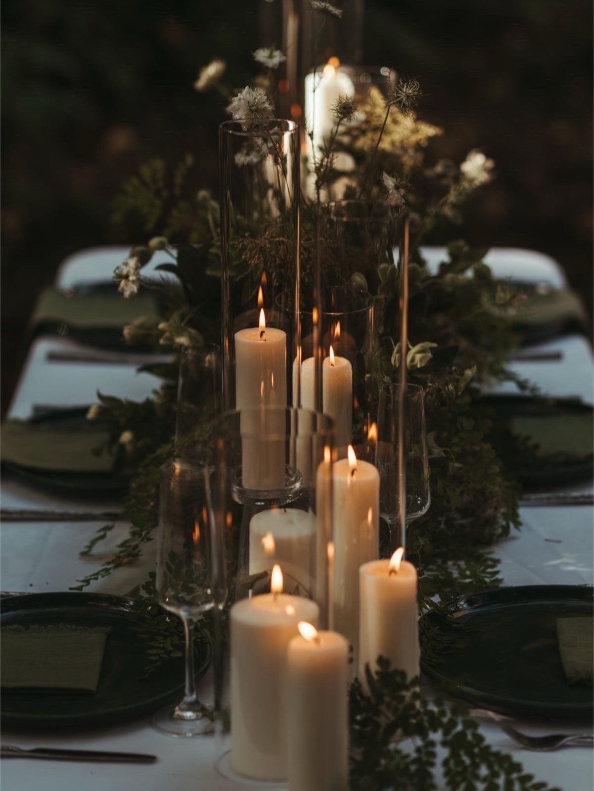 Candlelit wedding table runner with greenery and white flowers in a dark forest