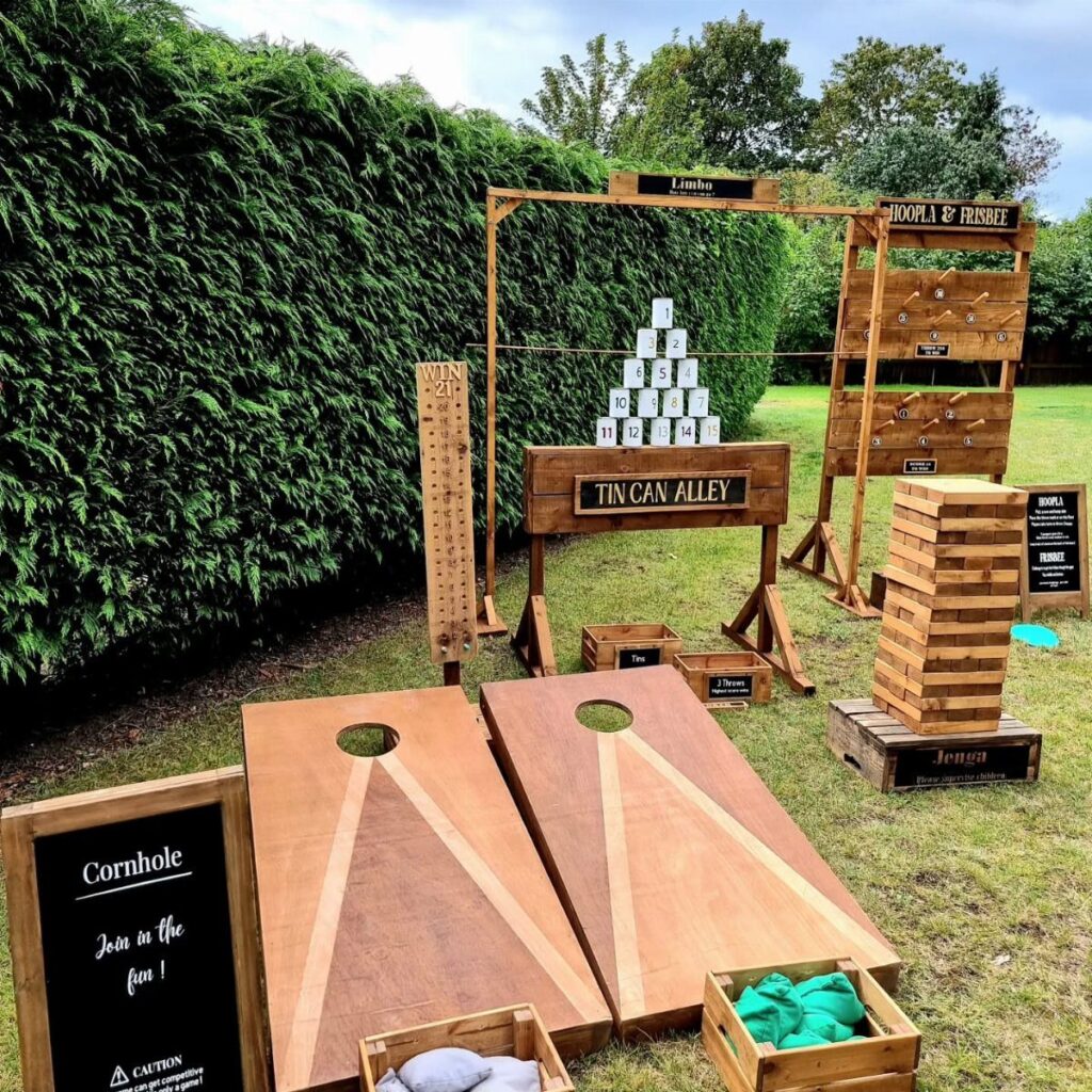 Wooden lawn games including cornhole and Jenga set up on a grassy garden lawn.