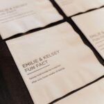 White cocktail napkins with printed fun facts about a couple on dark wood.
