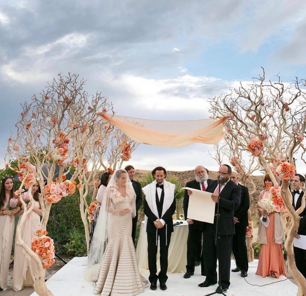 Bride and groom standing under a chuppah during a Jewish wedding ceremony outdoors.