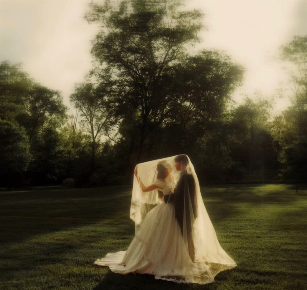 Bride and groom under a veil in a field with vintage sepia tones.