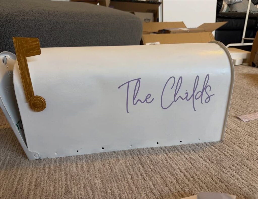 White metal mailbox with purple cursive text and gold flag on beige carpet