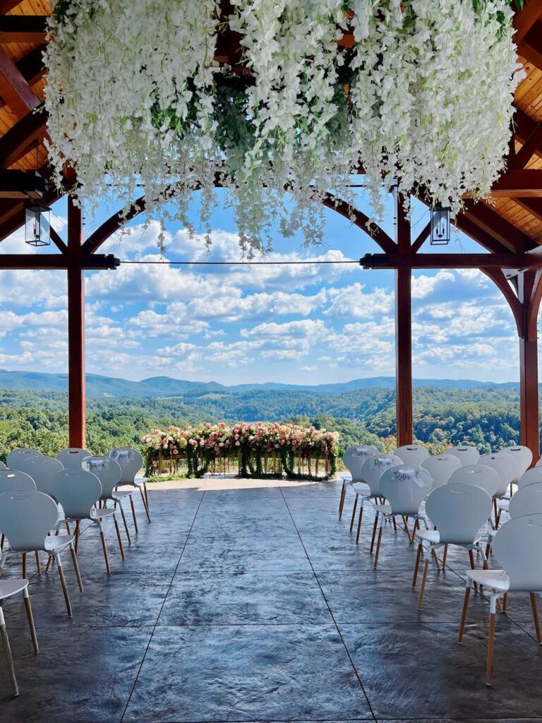 Wedding ceremony setup with white chairs and floral altar overlooking green mountain vistas.