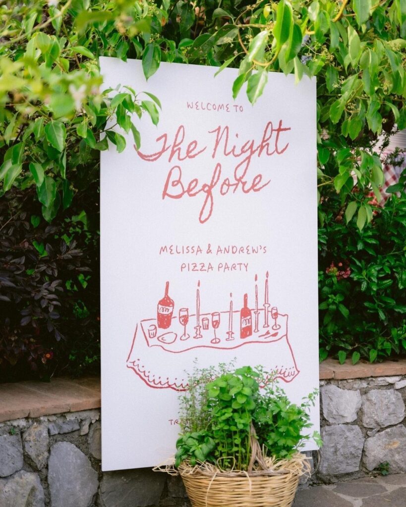 Welcome sign for a pizza party placed outdoors among green leaves and stones.