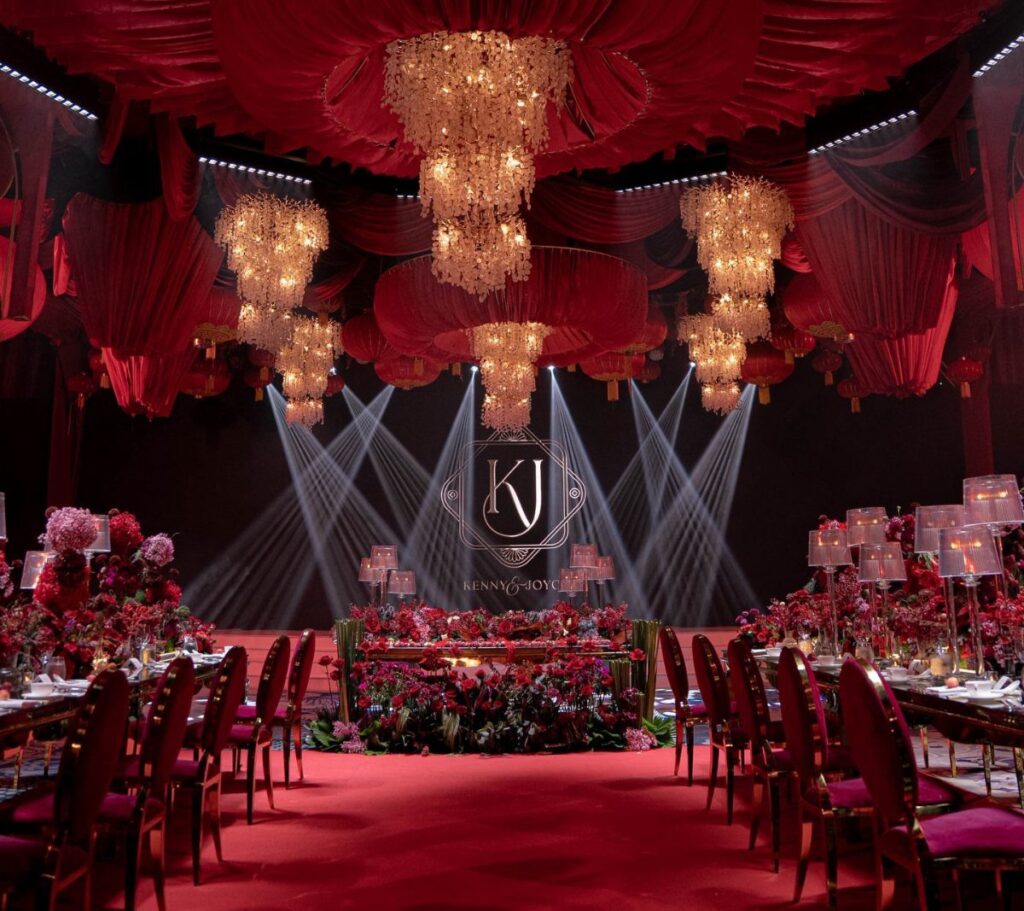Luxurious red carpet event space with red drapery, crystal chandeliers, and floral tables.