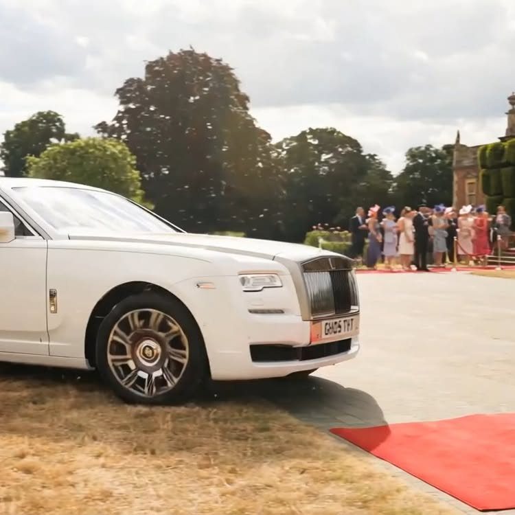 White Rolls Royce parked by a red carpet with wedding guests in background