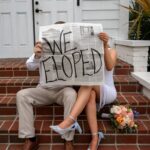 Couple sitting on brick steps holding a newspaper that says WE ELOPED