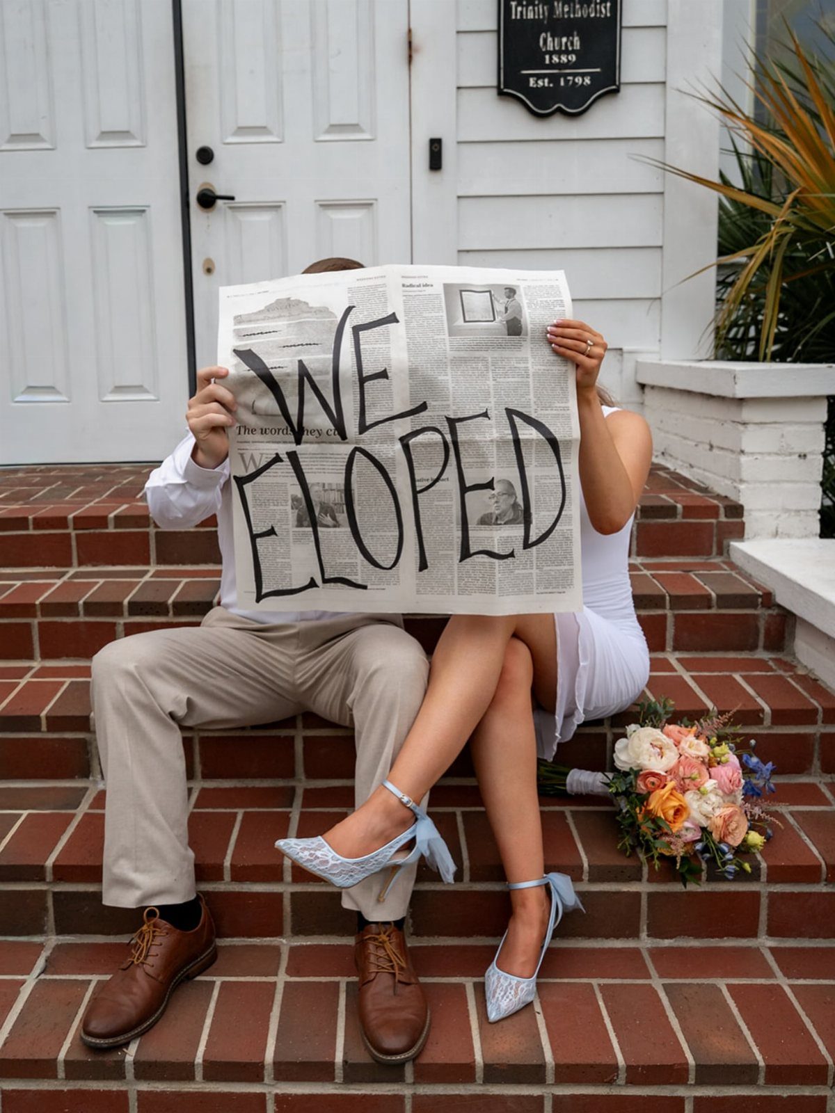 Couple sitting on brick steps holding a newspaper that says WE ELOPED