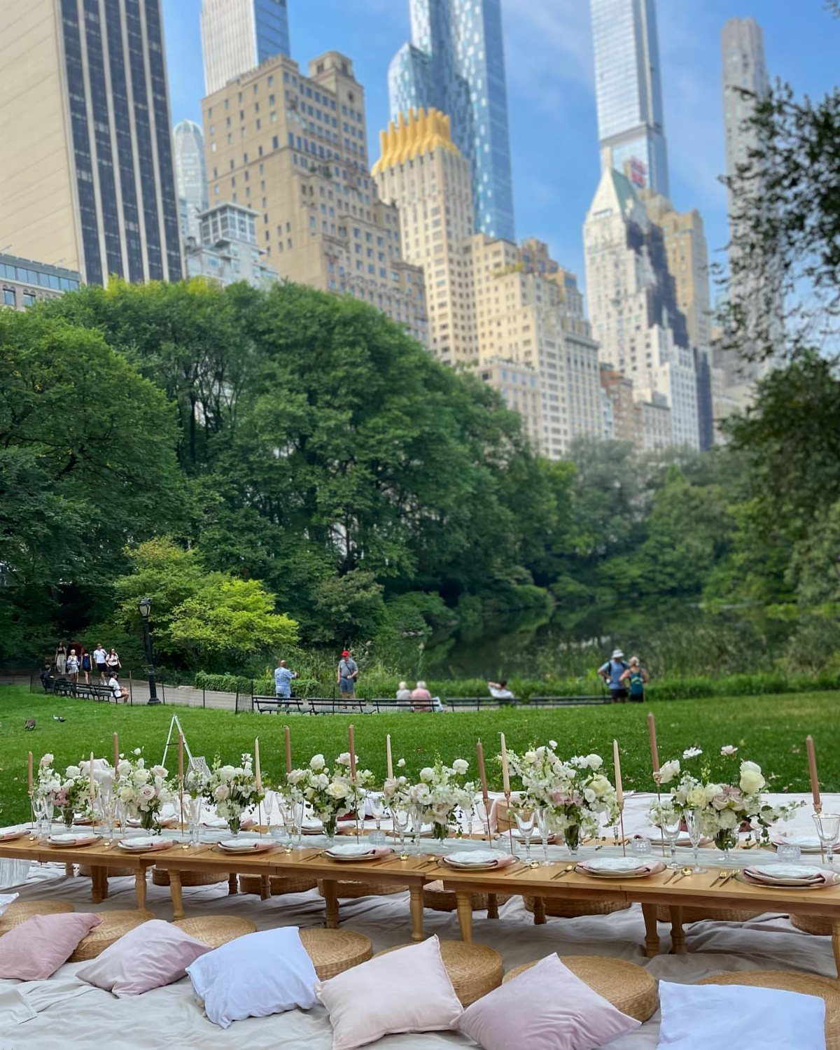 Formal outdoor dining table with white flowers set in a park with skyscrapers.