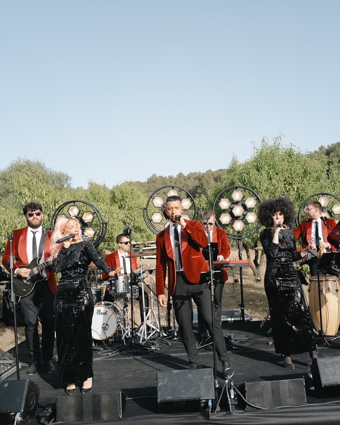 Live band in red velvet blazers performing on an outdoor stage with lights.