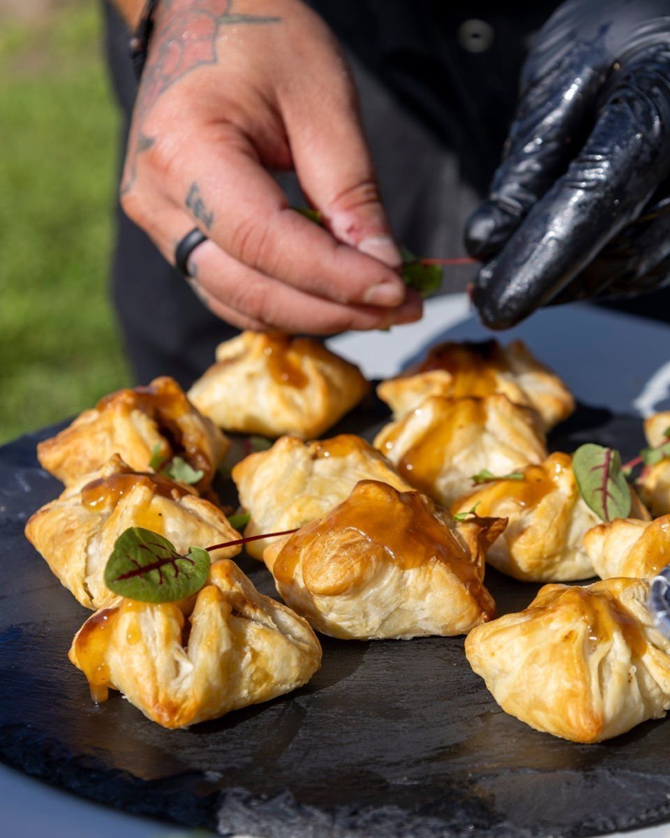 Golden-brown glazed pastry appetizers on a slate platter being garnished with microgreens.