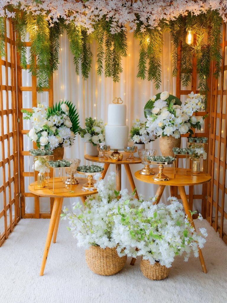 Wooden wedding pergola decorated with white flowers and greenery over a cake table.