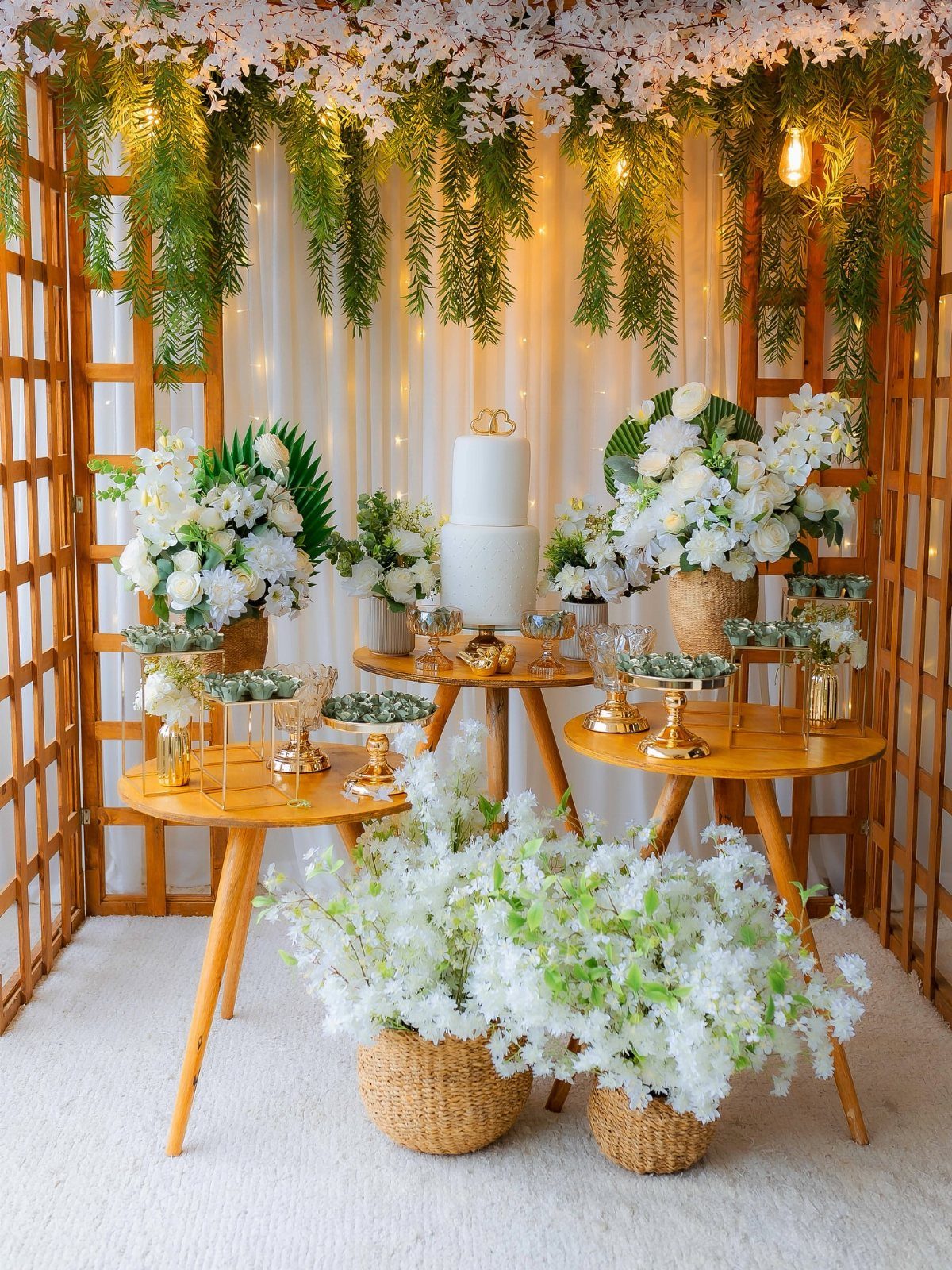 Wooden wedding pergola decorated with white flowers and greenery over a cake table.