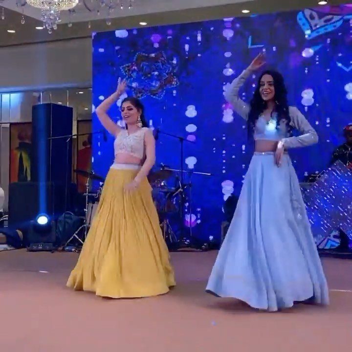 Two women in colorful lehengas dancing on a stage at a wedding reception.