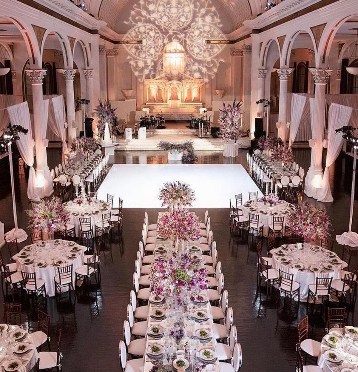Grand wedding reception layout with white tables, purple flowers, and a central dance floor.