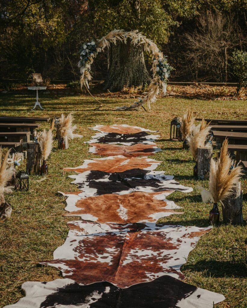 Cowhide rug aisle leading to a pampas grass circular arch in a forest
